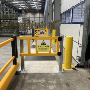Yellow pedestrian safety gate with steel posts beside a warehouse loading bay, polymer barrier and zebra crossing in view.
