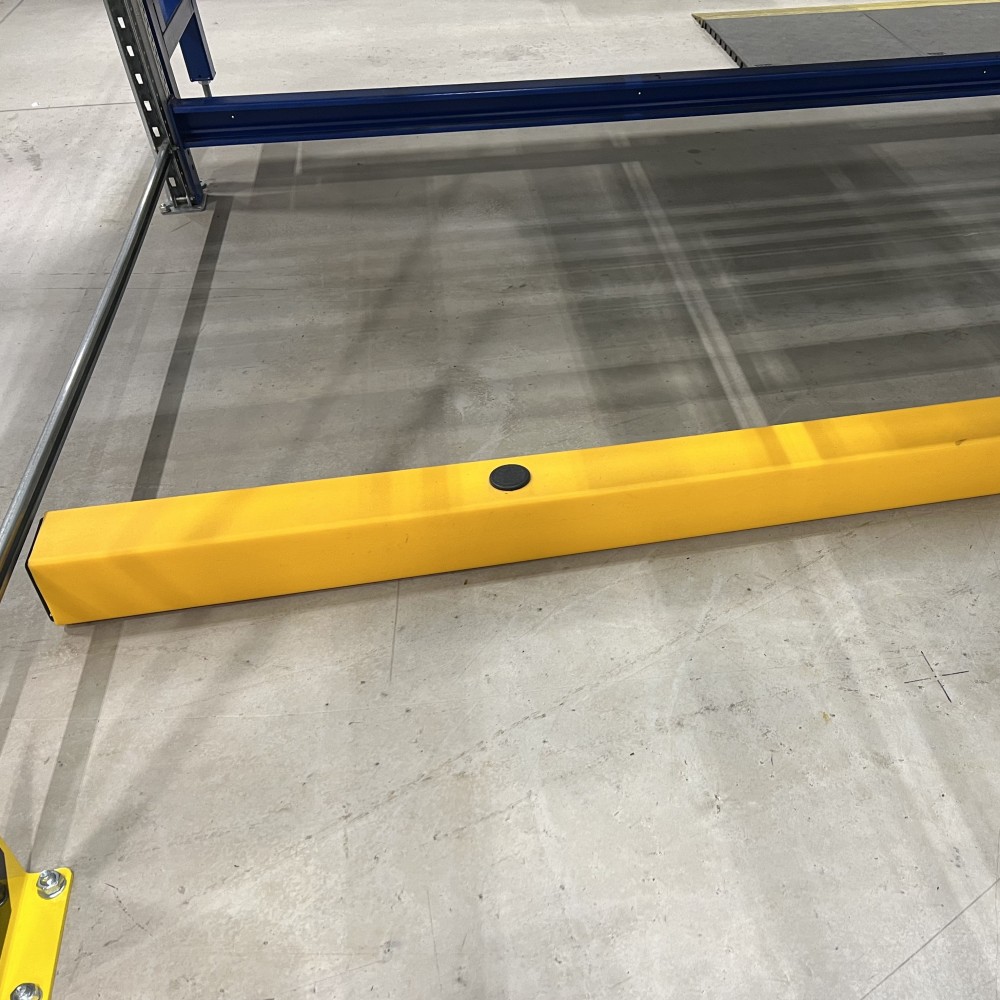 Close-up of a safety yellow floor rail bumper installed beneath machinery and racking to protect uprights and equipment from forklift and MHE damage.